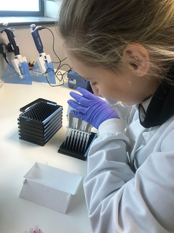 Close-up of woman in a white lab coat and gloves using a pipette to insert samples into test beds